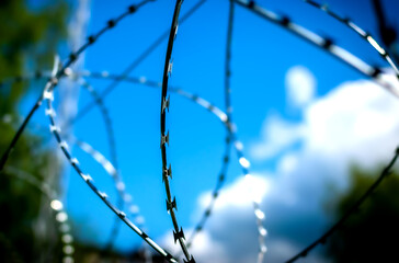 A fence with barbed wire in front of a clear blue sky.  barrier of the forbidden zone.