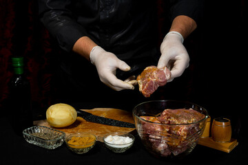 Marinating raw pork for cooking kebabs and ham. The chef of the restaurant in gloves treats the meat with basil and curry spices.