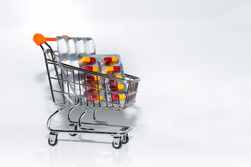 Miniature shopping cart filled with tablets and capsules on a white background, medicine and Coronavirus concept.