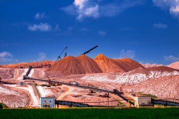 Industrial background. Salt mining site under blue bright sky. Large excavator machine and Huge mountains of waste ore in the extraction of potassium.