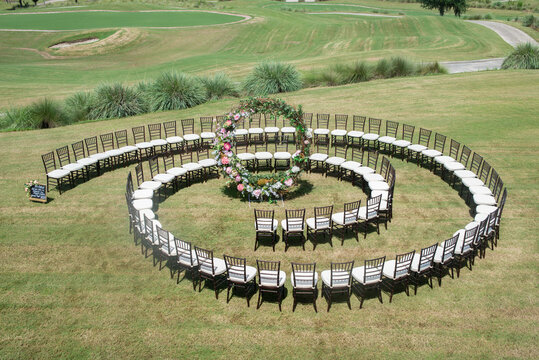 Unique round spiral chair pattern wedding ceremony setting at rolling hills countryside with brown chiavari chairs and white cushions