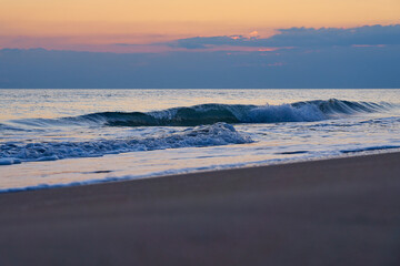 Sandy beach on a sunset with reflection on wet sand and waves with foam. Copy space.