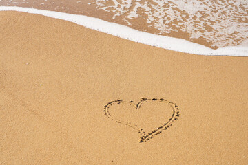 A heart symbol written on a sandy beach with foam and water background. Valentines day concept.