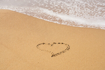 A heart symbol written on a sandy beach with foam and water background. Valentines day concept.