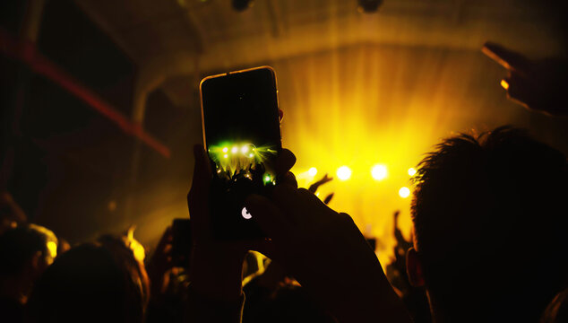 smartphone in the hand of a fan shooting videos and photos from the crowd at a concert of his favorite artist. The atmosphere of a music festival with a cool lit scene. show banner
