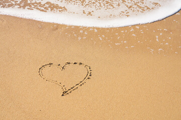 A heart symbol written on a sandy beach with foam and water background. Valentines day concept.