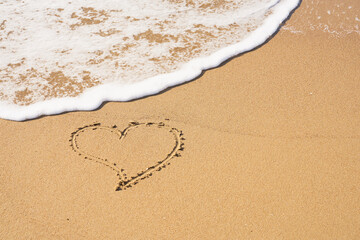 A heart symbol written on a sandy beach with foam and water background. Valentines day concept.