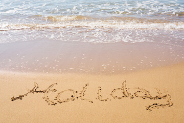 Holiday inscription on a tropical sandy beach with waves and foam on a background.