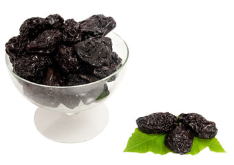 prunes in a glass bowl with green leaves isolated on white background