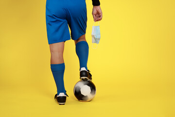 football player with face mask in hand and ball in foot