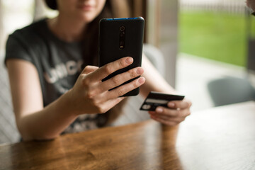 Online payment. Woman 's hands holding a credit card and using smart phone for online shopping. Indoor close-up. Online shopping concept