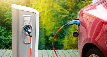 Close-up of an electric car with a cable connected and a charging station - obrazy, fototapety, plakaty