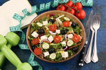 Authentic fresh salad in a stone cup with dumbbells excercise equipment, measuring tape on table. healthy lifestyles, good health Concept with fresh ingredients