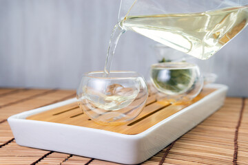 pours chinese green tea from glass kettle to small cup. close up selective focus