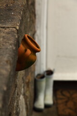 an outdoor decoration containing a broken clay vase on the wall and vintage boots in the background