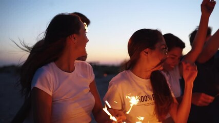 Friends walking, dancing, having fun at night party at the seaside with sparklers in their hands. Young teenagers partying on the beach with fireworks and bengal lights. Slow motion steadycam shot. - Powered by Adobe