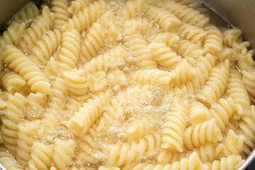 Boiling fusilli macaroni in a pot on an electric stove close up. Steam and Bubbling of hot water.