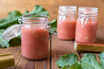 selbstgemachter gekochter rosa roter Rhabarbermus mit Stücken im Glas auf einem braunen Tisch aus Holz