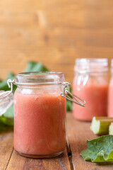 selbstgemachter gekochter rosa roter Rhabarbermus mit Stücken im Glas auf einem braunen Tisch aus Holz