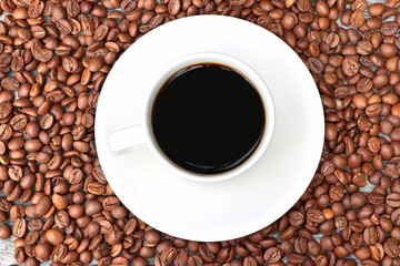 A cup of coffee and coffee beans on a wooden background. Heap of coffee beans. White coffee cup and saucer.