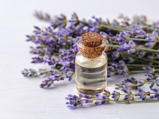Close-up of lavender essential oil in a glass bottle and fresh fragrant lavender on a white wood surface. Home made spa, skincare and cosmetology concept.