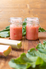selbstgemachter gekochter rosa roter Rhabarbermus mit Stücken im Glas auf einem braunen Tisch aus Holz
