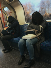 Two tired passengers, a woman and a man, head bowed asleep on the London underground train, their...