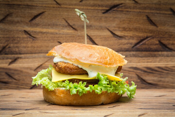 burger with chicken, cheese and salad on a wood brown board