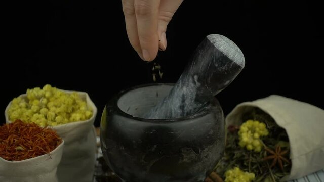 Woman's hand puts cumin seeds into the granite mortar with pestle in slow motion. Healthy and organic food, herb medicine, natural care, aromatherapy and organic cosmetics concept.
