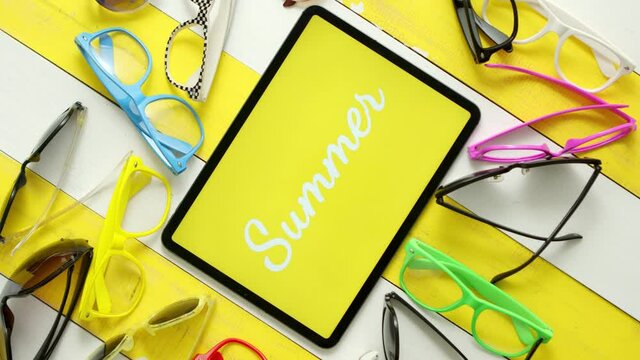 Various style, shape and colour sunglasses. Tablet in the middle with text SUMMER.