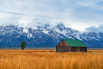 Fototapeta na wymiar Grand Teton Range Peaks in the first snow and mist in autumn with a building of the T. A. Moulton barn inside Grand Teton National Park, Wyoming,United States of America (USA).