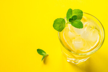 Glass with lemonade or mojito cocktail with lemon, mint and ice over yellow background. copy space.