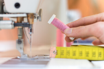 Pink thread in a dressmaker workshop: Close up tailor hands holding a pink thread