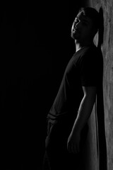 A dark silhouette of a man stands against the wall. Black and white portrait. Sadness, depression. Gaze into the distance. Black clothes.