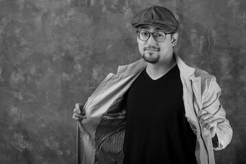 Fototapeta premium A man with glasses poses in a jacket and a flat cap. Smile, joy. Black-and-white portrait of a person.