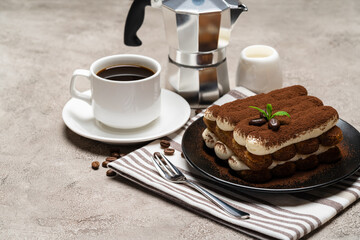 Classic tiramisu dessert on ceramic plate, milk or cream and cup of coffee on concrete background