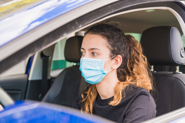 New normal. Female driver with a medical face mask driving a car with a passenger. Health protection. Family in the car protected by a mask safety and pandemic concept. Coronavirus. Social distance.