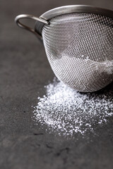 Close up of powder sugar in a mesh strainer sitting on a table top
