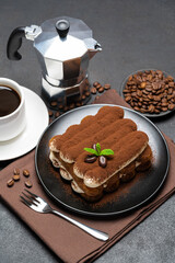 Classic tiramisu dessert on ceramic plate, milk or cream and cup of coffee on concrete background