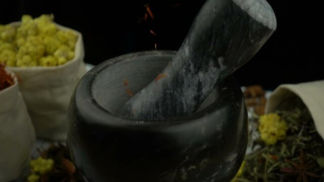 Herbs and flowers falling into the granite mortar with pestle in slow motion. Healthy and organic food, herb medicine, natural care, aromatherapy and organic cosmetics concept.
