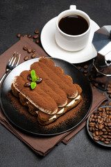 Classic tiramisu dessert on ceramic plate, milk or cream and cup of coffee on concrete background