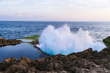 Wave breaking on the western Kona coast of Hawaii's Big Island. Spray and foam in foreground. Pacific ocean, sky with clouds beyond. 
