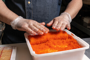 The chef rolls a roll in orange caviar