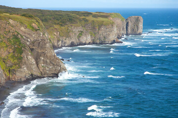 Beautiful ocean view from the edge of the cliffs on Kamchatka Peninsula, Russia. Deep blue sea water of Pacific ocean, beach with black sand, mountains and autumn landscape.