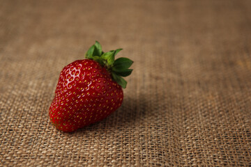 Ripe red strawberry on burlap background. Space for text.