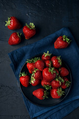 Ripe red strawberries in a black plate with blue napkin on dark blue background. Sweet dessert from fresh berries on the table.