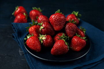 Ripe red strawberries in a black plate with blue napkin on dark blue background.