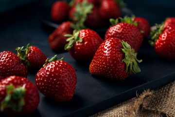 Ripe red strawberries with black serving board on burlap and dark blue background. Sweet dessert from fresh berries on the table.