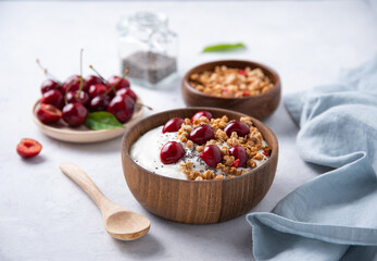 natural fermented yogurt with granola, chia seeds  and  fresh cherry in wood bowl on light table
