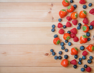 Naklejka na ściany i meble Strawberries, blueberries and raspberries as border on wooden background